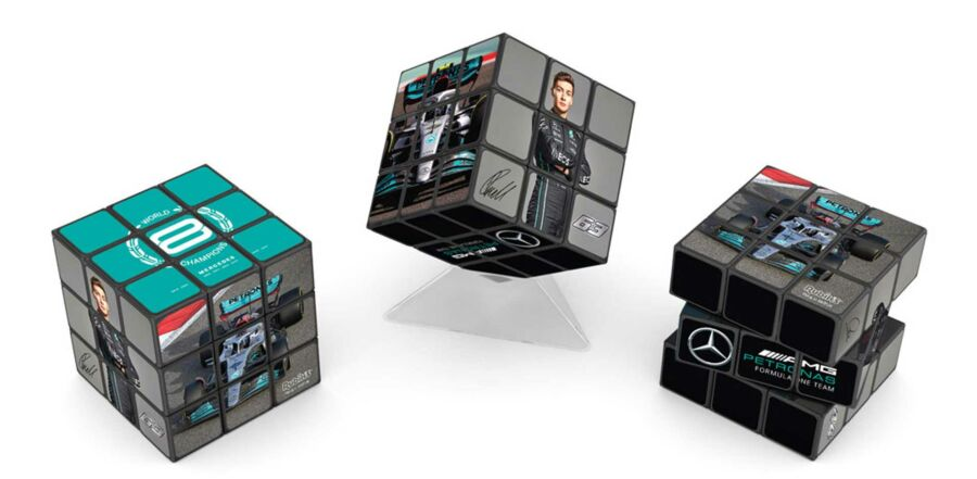Három Rubik-kocka, Formula 1-es versenyképekkel és logókkal, fehér háttérben lebegve.