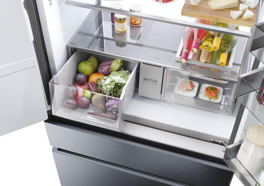 Geöffneter Kühlschrank mit Obst und Gemüse in Schubladen und verschiedenen Lebensmitteln in Regalen.
