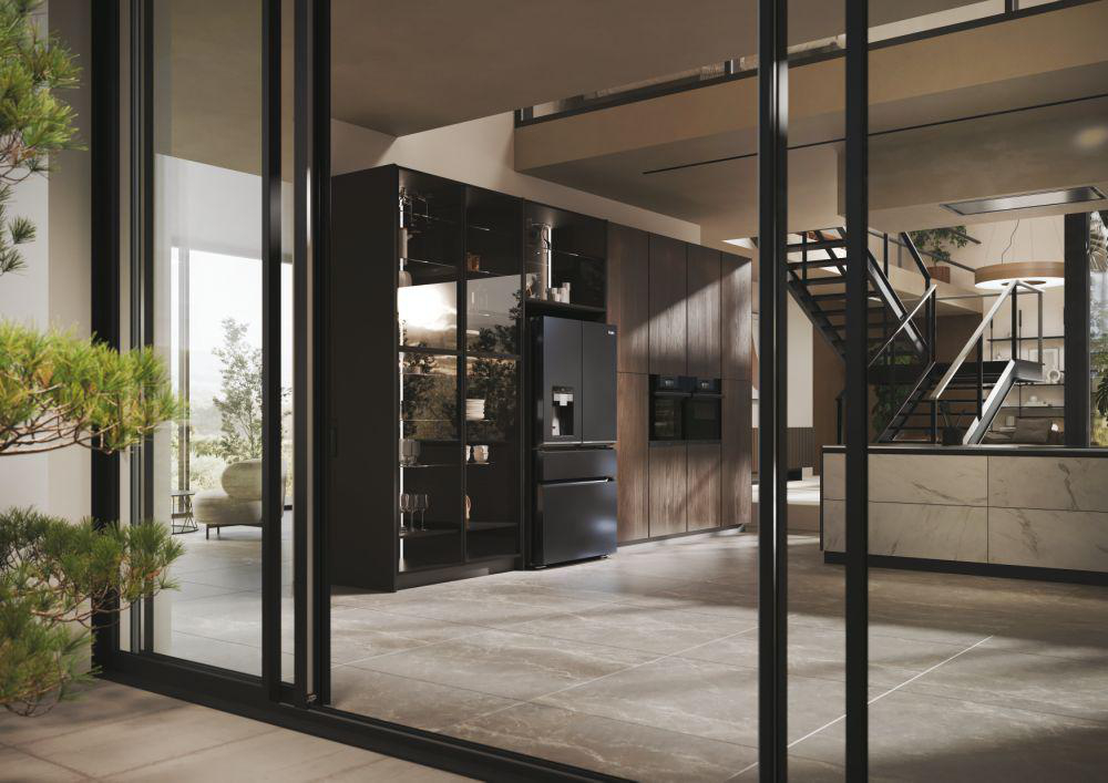 Außenansicht einer modernen Küche. Schwarzer Kühlschrank, Glastüren, Holzschränke, Treppe sichtbar.