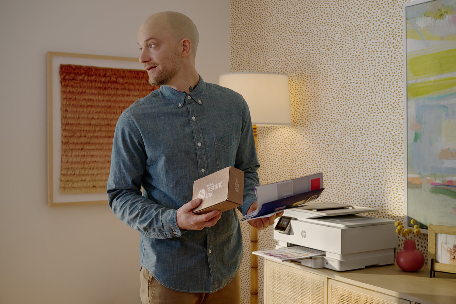 Man met doos en papieren, staat bij een printer op een kast.