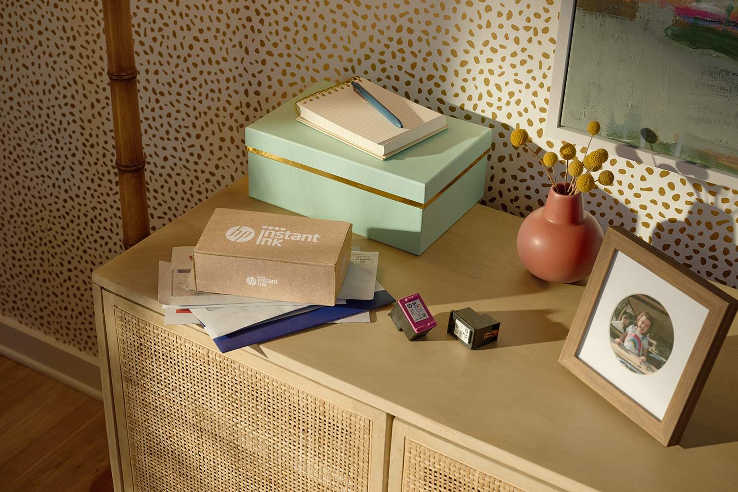 Een bureau met kantoorbenodigdheden: een doos, een notitieboek, een pen, een vaas met bloemen en een ingelijste foto.