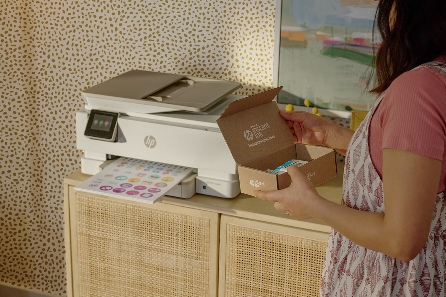 Vrouw die een doos met instant inktpatronen vasthoudt bij een printer op een kast.