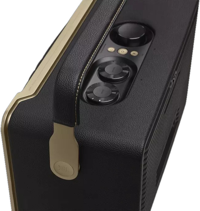 Haut-parleur portable noir et doré, gros plan. Poignée, commandes en haut. Logo JBL sur le côté.