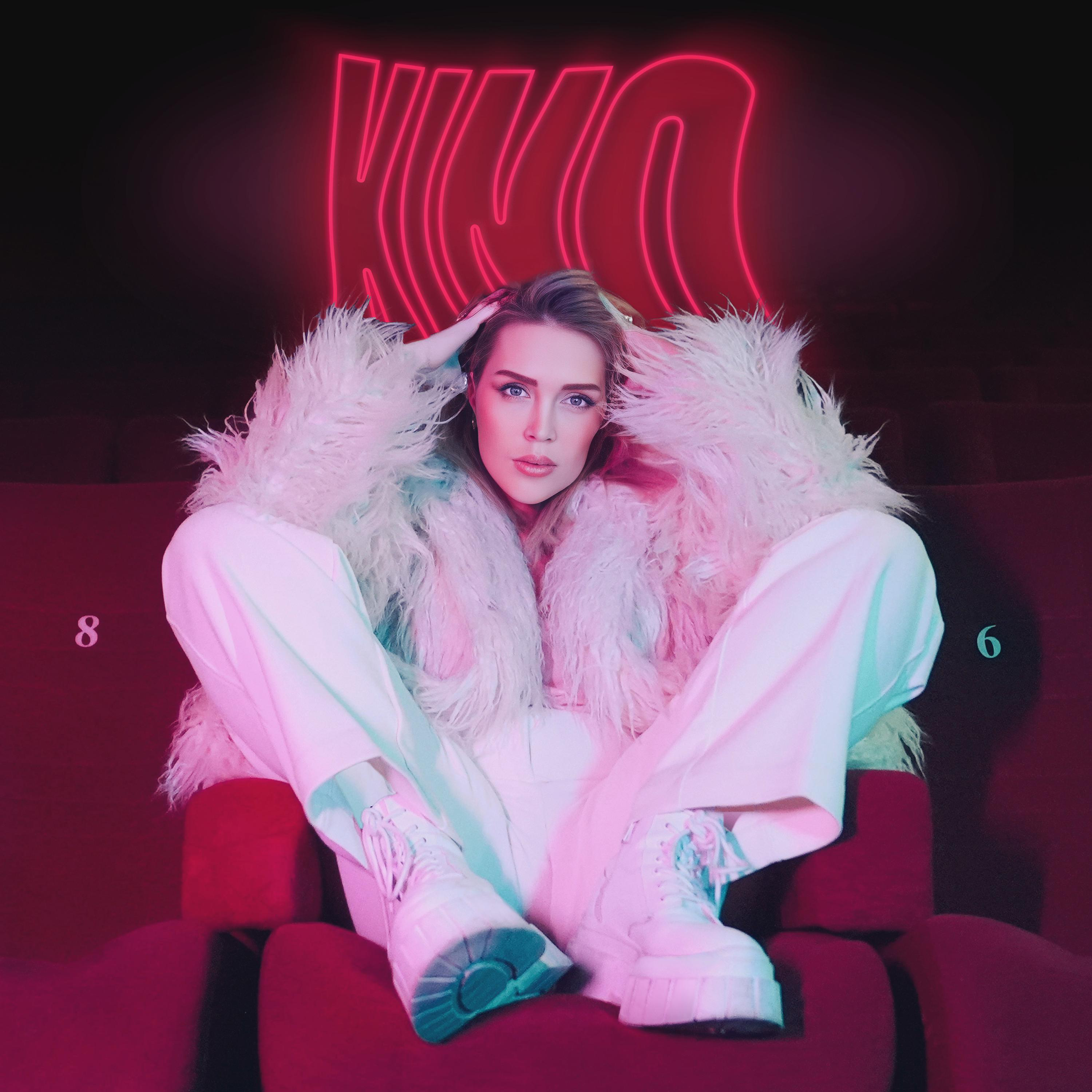 Frau in weißem Outfit und Pelzmantel sitzt in rotem Theatersitz, Neon-Schild mit NIKA, 8 und 6.