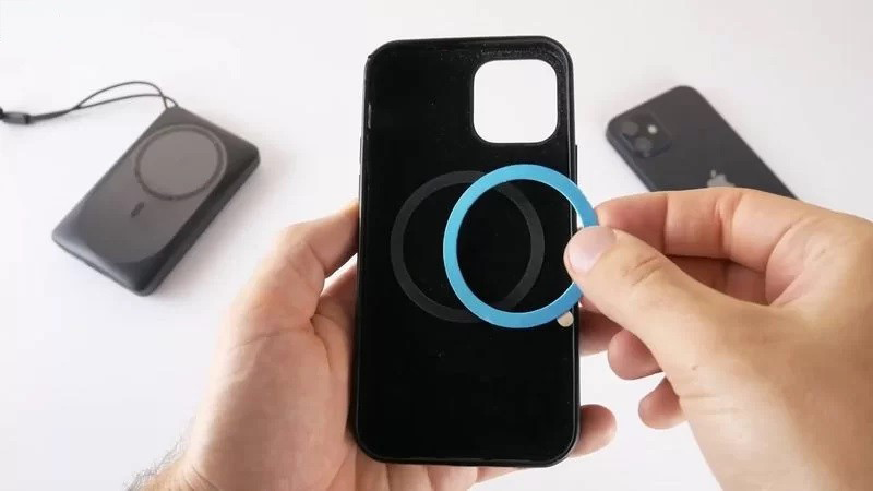 Egy személy kék gyűrűt szerel össze egy fekete telefontokon. Egyéb telefontartozékok vannak.