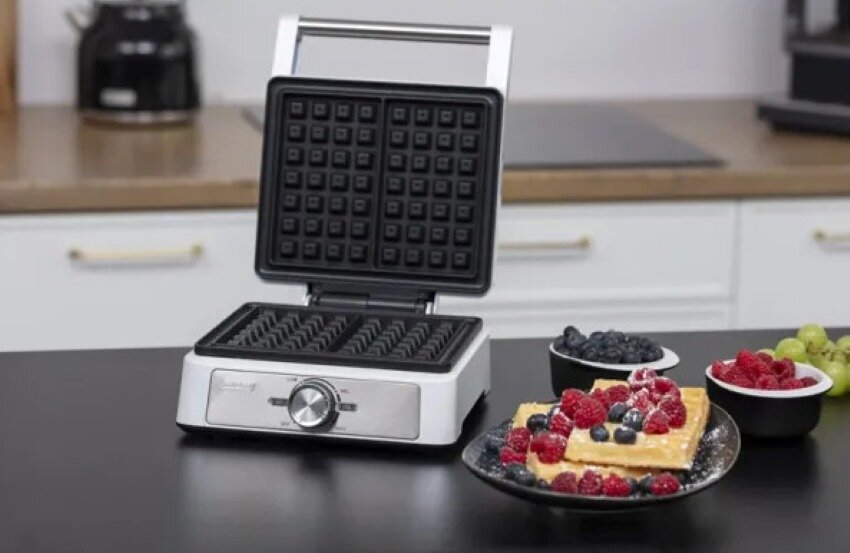 Gofrownica z goframi i jagodami na stole. Czarno-biała kuchnia w tle.