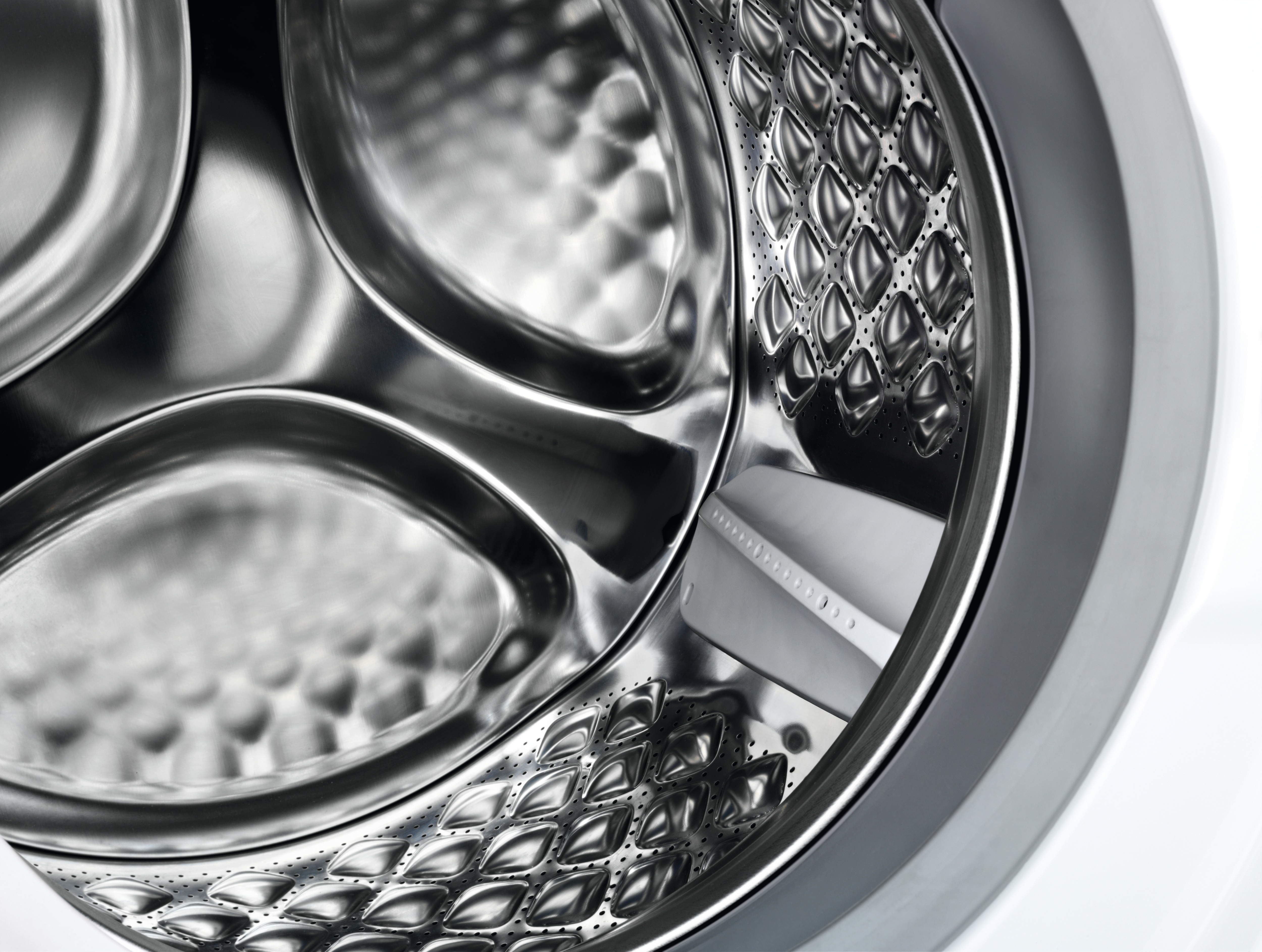 Gros plan de l'intérieur du tambour d'une machine à laver, acier inoxydable et motif de trous.