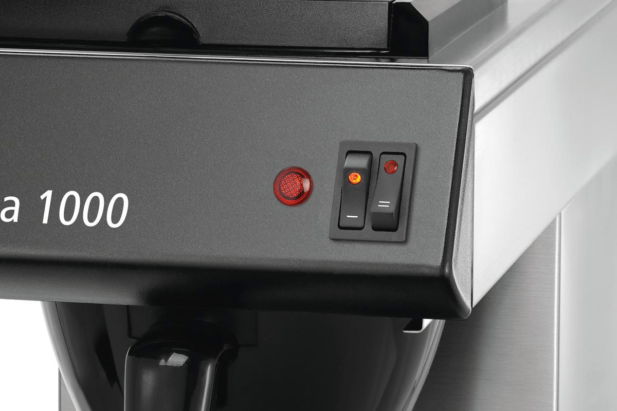 Nahaufnahme eines Bedienfelds einer Kaffeemaschine. Es hat ein rotes Licht und zwei schwarze Schalter. Die Oberfläche ist dunkelgrau.