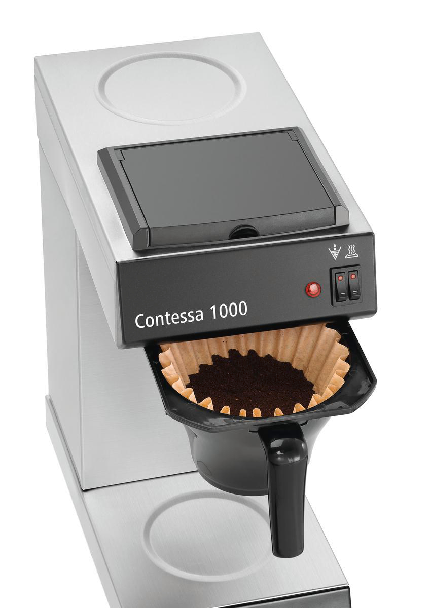 Eine Contessa 1000 Kaffeemaschine. Sie hat eine schwarze Front mit dem Namen, einem roten Licht und zwei Schaltern. Ein Filter mit Kaffeepulver.