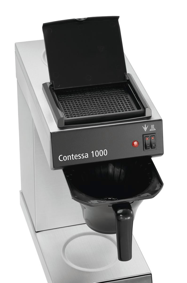 Eine Kaffeemaschine Contessa 1000 ist abgebildet. Sie hat einen schwarzen Deckel, einen schwarzen Filterkorb und einen schwarzen Kaffeekannenhalter. Der Körper ist silberfarben.