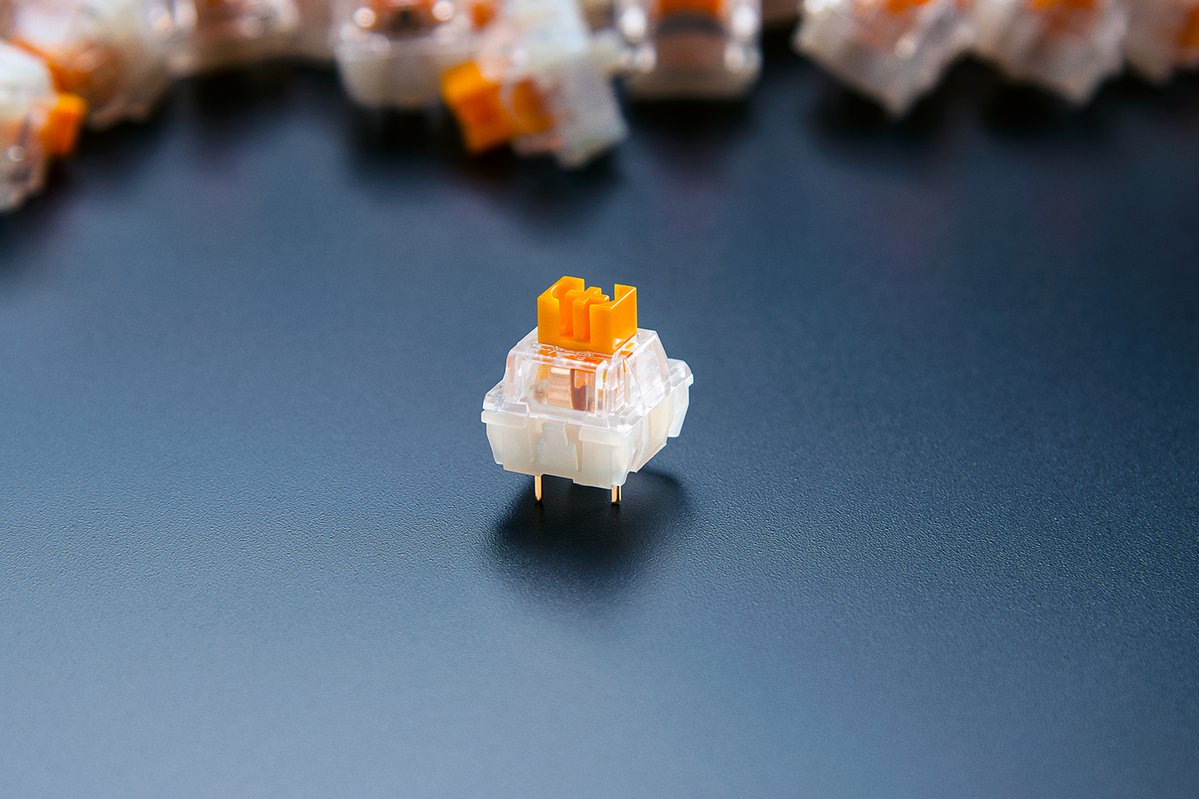 Ein einzelner mechanischer Tastaturschalter. Er ist weiß und orange auf einer dunklen Oberfläche.