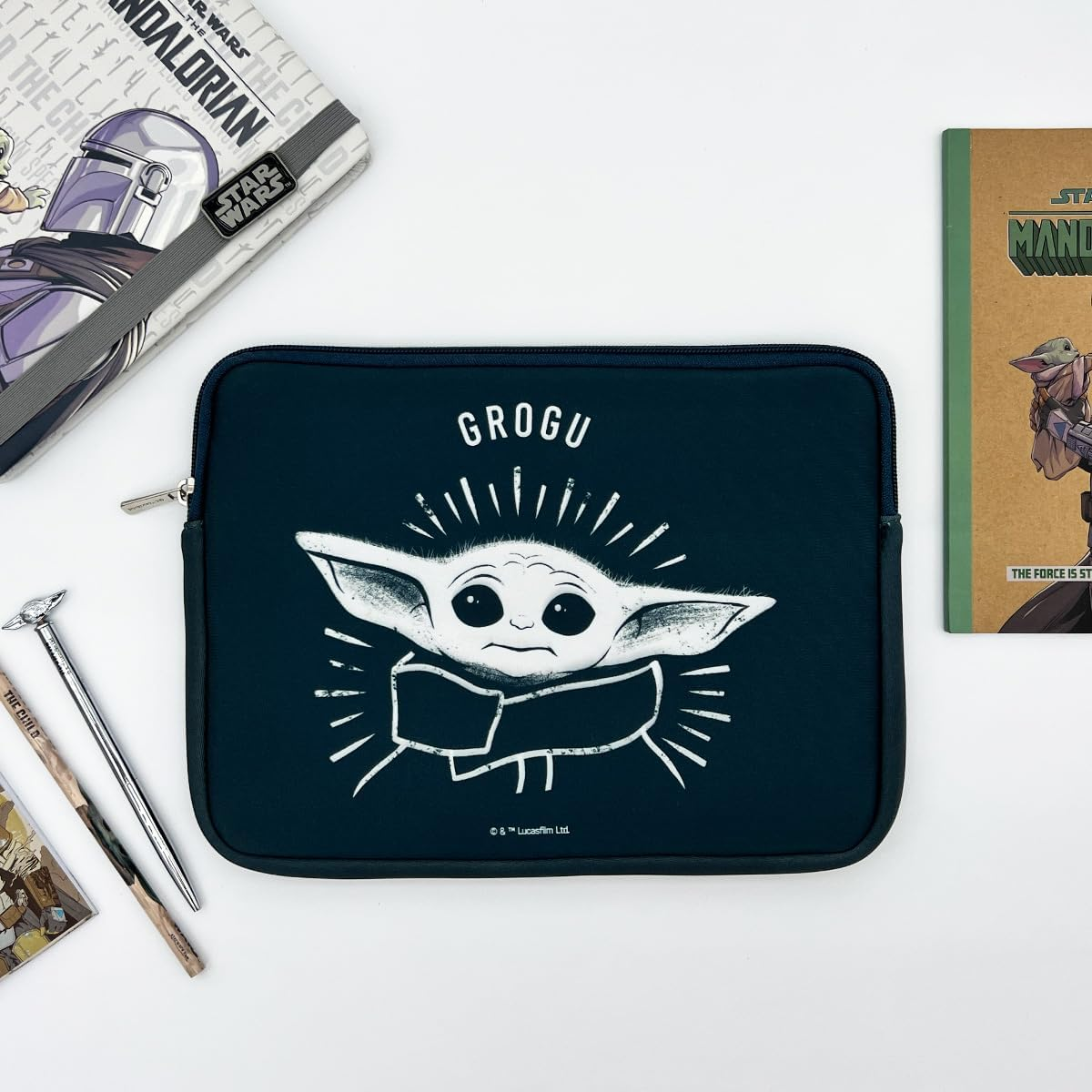 Una funda para portátil Grogu con accesorios de Star Wars sobre una superficie blanca.  Con la imagen de Grogu.