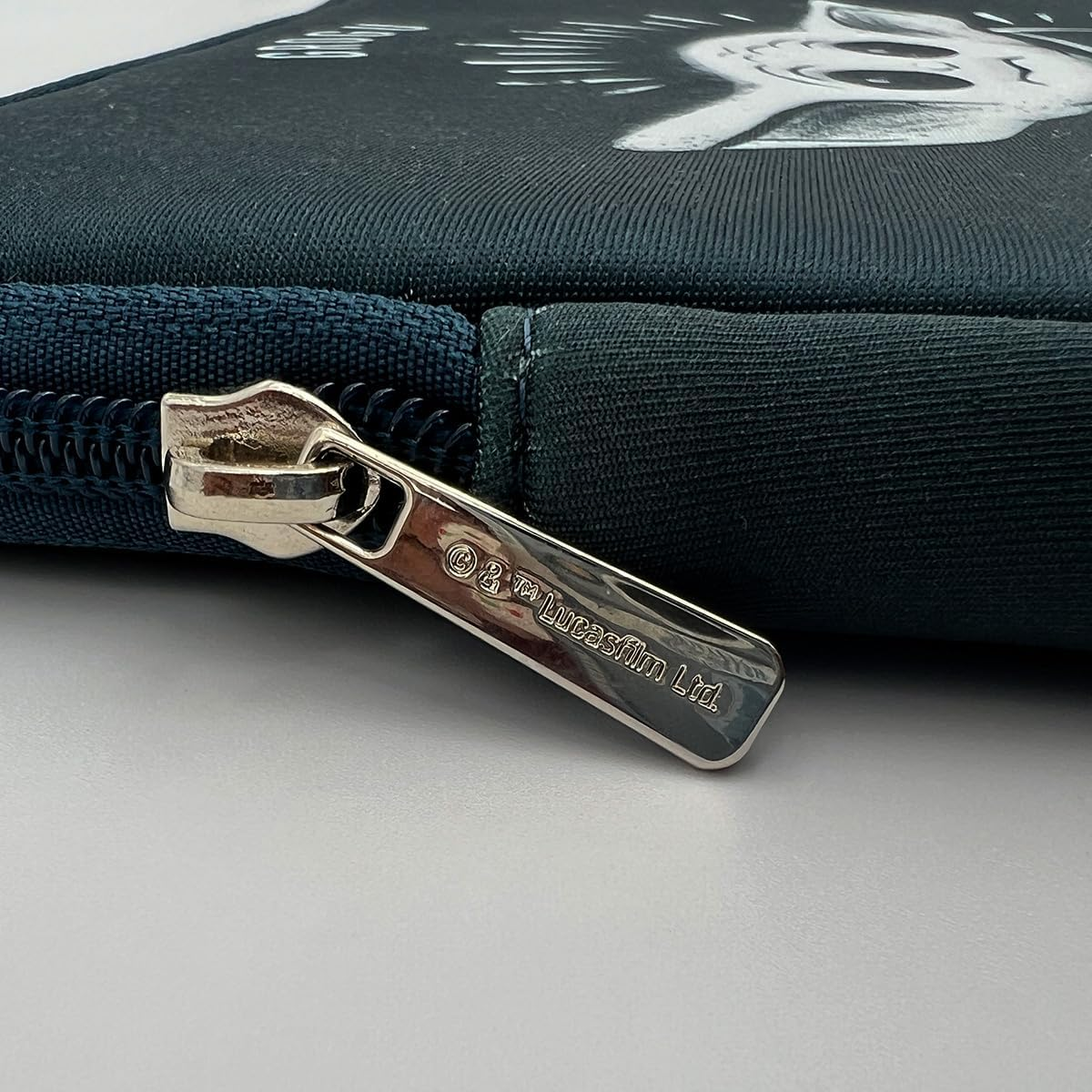 Primer plano de una funda para portátil azul marino con cremallera. Hay un gato de dibujos animados blanco en la funda.