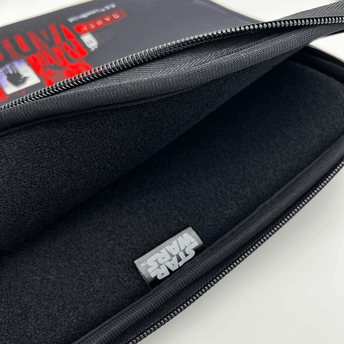 Funda negra para portátil con cremallera y etiqueta de Star Wars. Interior de tela negra. Fondo blanco.