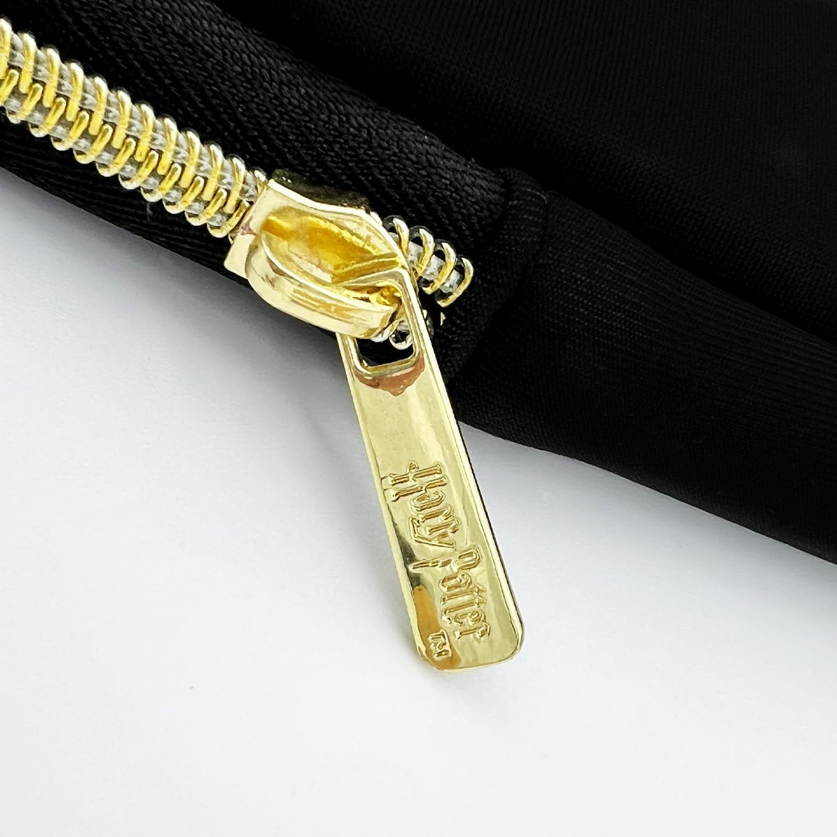 Primer plano de una cremallera de bolso negro con etiqueta dorada de Harry Potter.