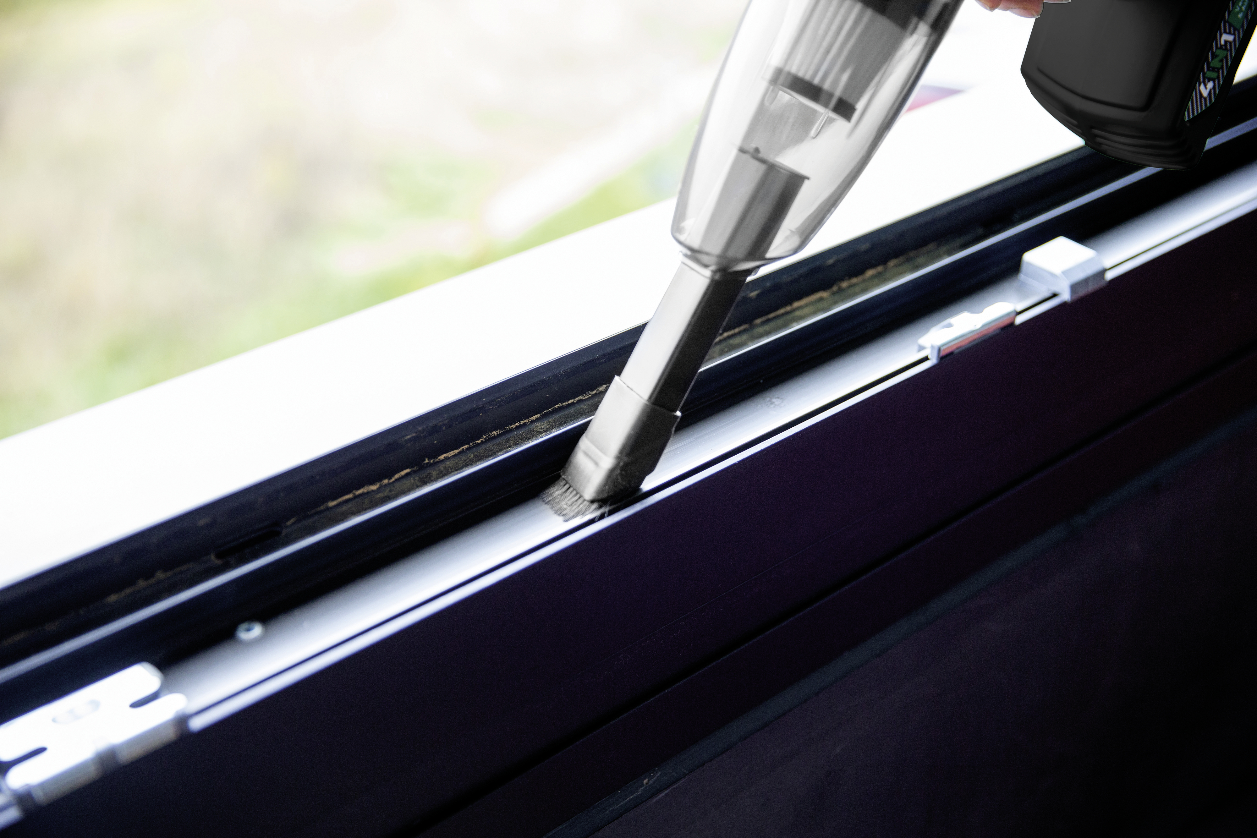 Ein Handstaubsauger saugt einen Fensterrahmen ab, Nahaufnahme.
