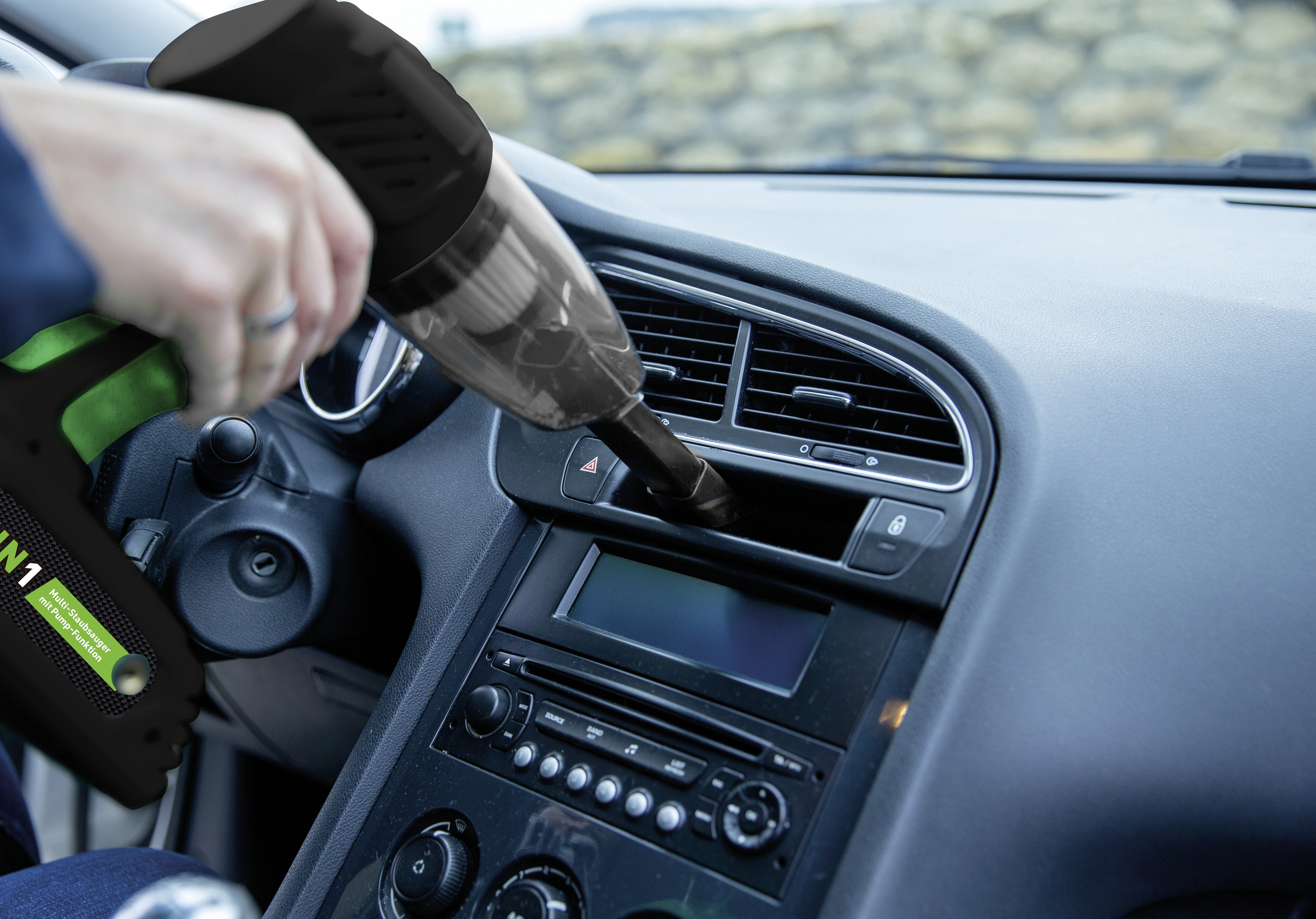 Hand, die einen schwarzen Staubsauger in einem Auto hält.