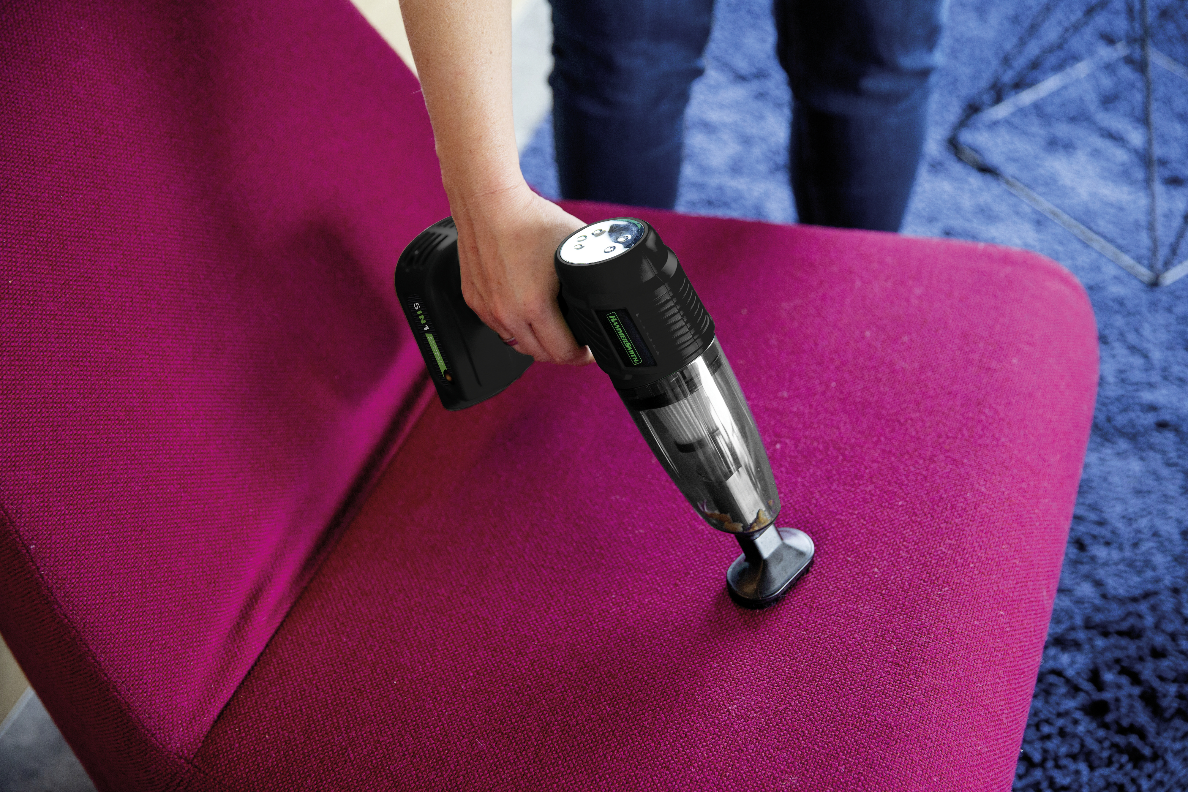 Eine Person benutzt einen Handstaubsauger auf einem magenta Stuhl.