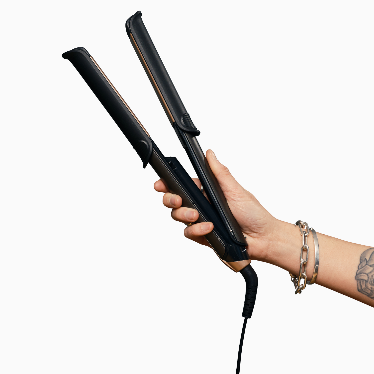 A hand holding a black and bronze hair straightener, isolated on a white background.
