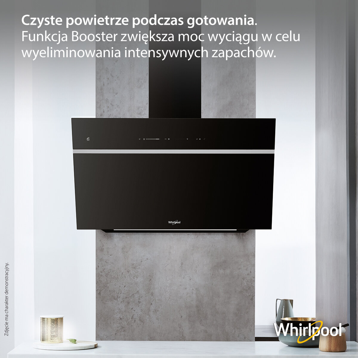 Czarny okap Whirlpool na szarej ścianie. Biały blat, metalowy dzbanek i złota świeca.