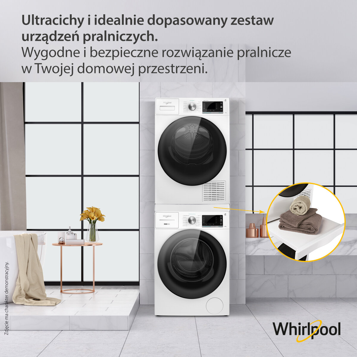 Dwie białe pralki ułożone jedna na drugiej, ręczniki i mały stolik z kwiatami w kafelkowanym pokoju.