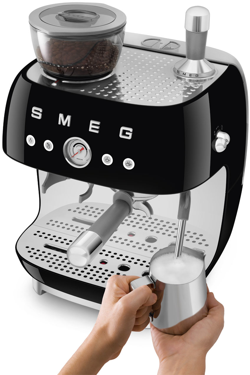 Una macchina per espresso Smeg nera con una mano che tiene una caraffa per montare il latte.