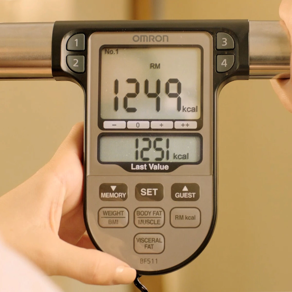 A testzsíranalizátor súly- és energiafelhasználási számokat jelenít meg. A képernyő szürke, a készüléket egy személy tartja.