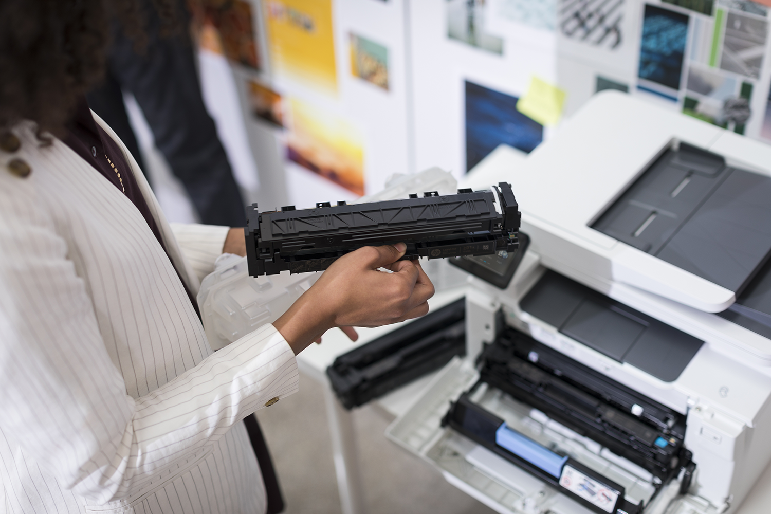 Person holding a black toner cartridge next to an open printer.