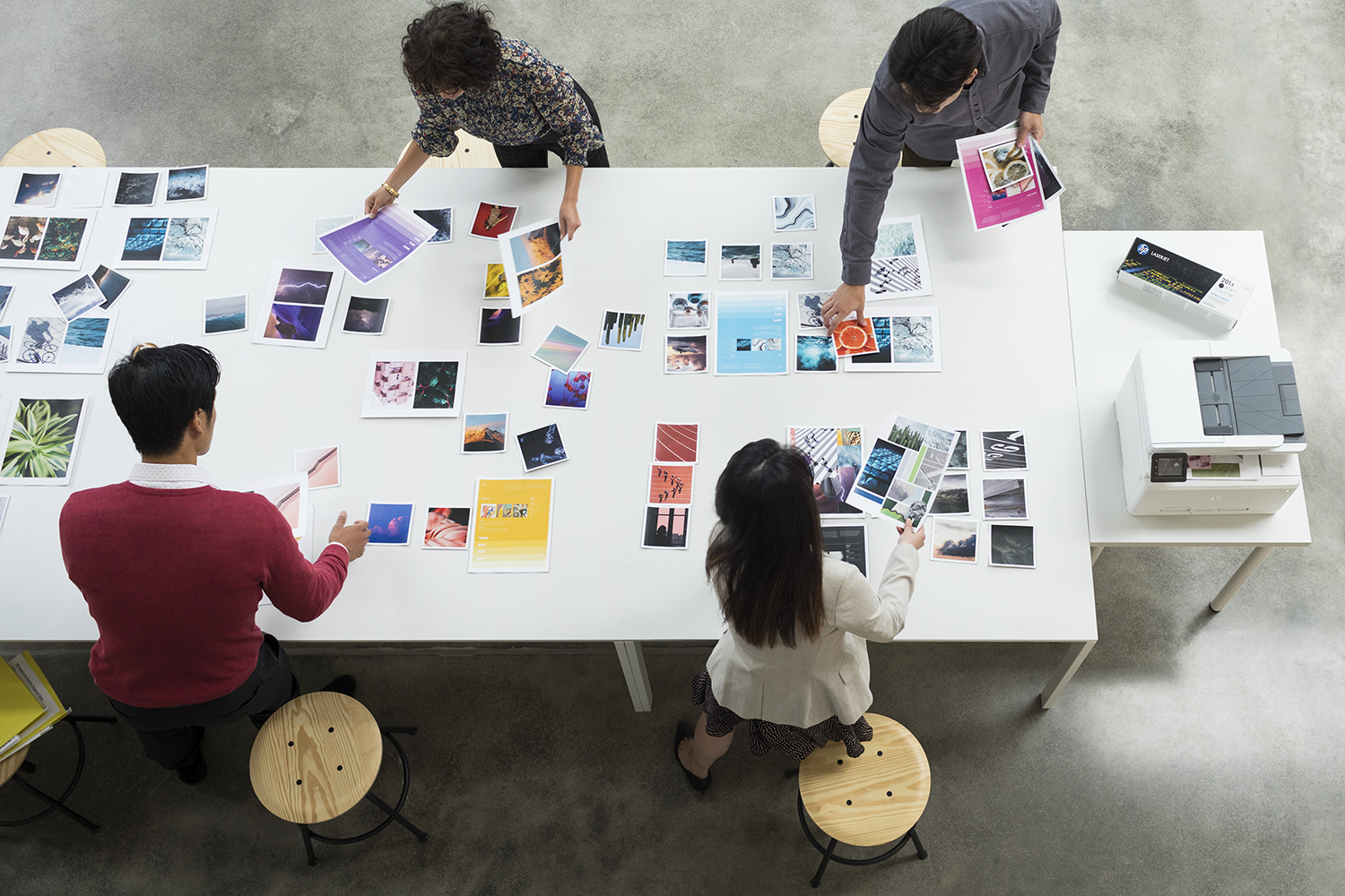 A team of people working at a table with photos, a printer, and a few stools.