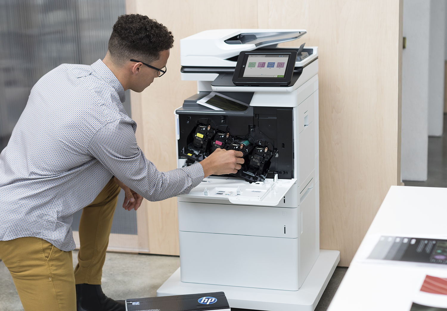 A man in glasses inserts ink cartridges into a white printer. Cartridges are yellow, magenta, and cyan.