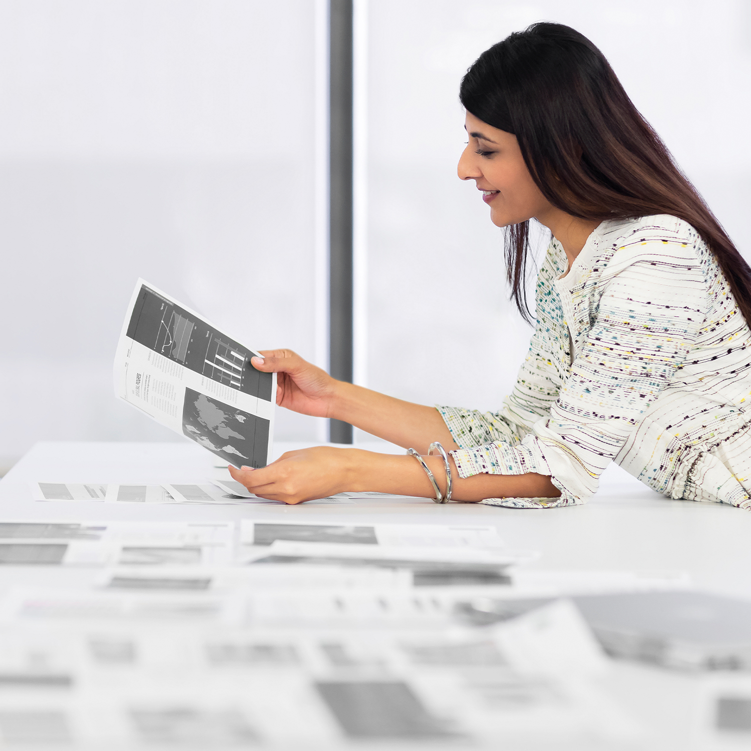 A woman examines charts and graphs on paper in a bright office setting.