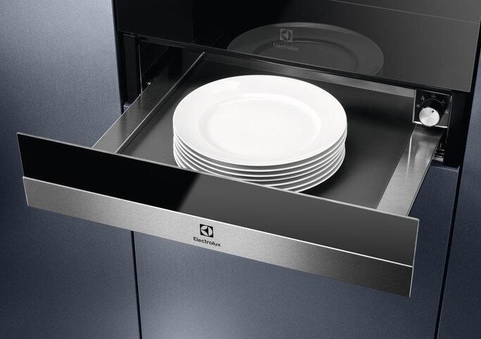 Szuflada ze stosem białych talerzy wewnątrz urządzenia kuchennego. Wykończenie ze stali nierdzewnej.