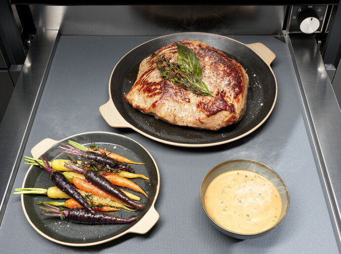 Talerz z pieczonym mięsem, marchewką i sosem. Wszystko na czarnej powierzchni.