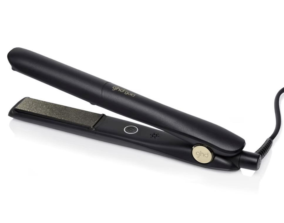Plancha de pelo negra 'ghd gold' sobre blanco. Cable negro adjunto. Logotipo dorado en el lateral.