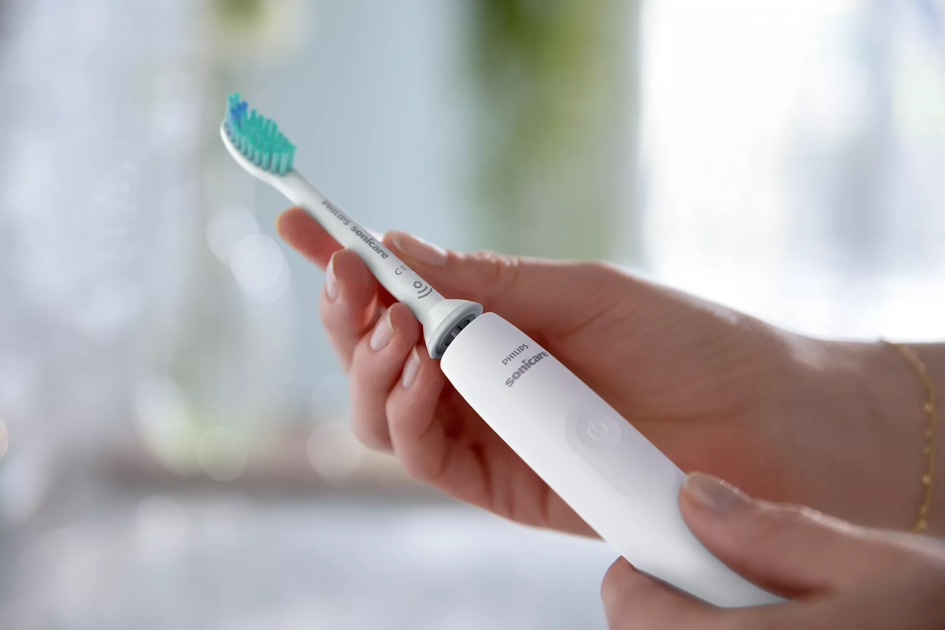 Kézben egy fehér Philips Sonicare fogkefe, zöld és kék sörtékkel.