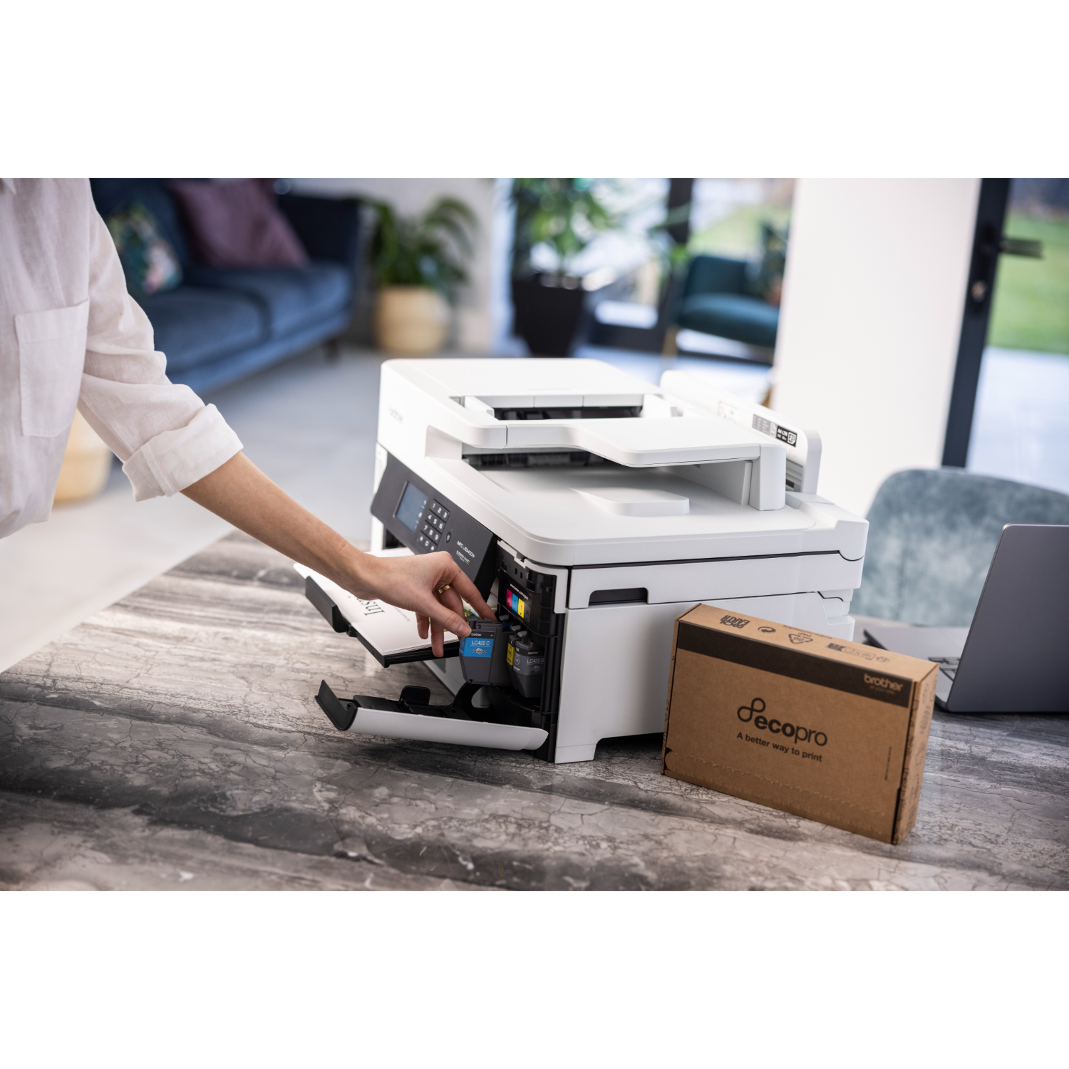 Person inserting a yellow and cyan toner cartridge into a white printer on a desk.