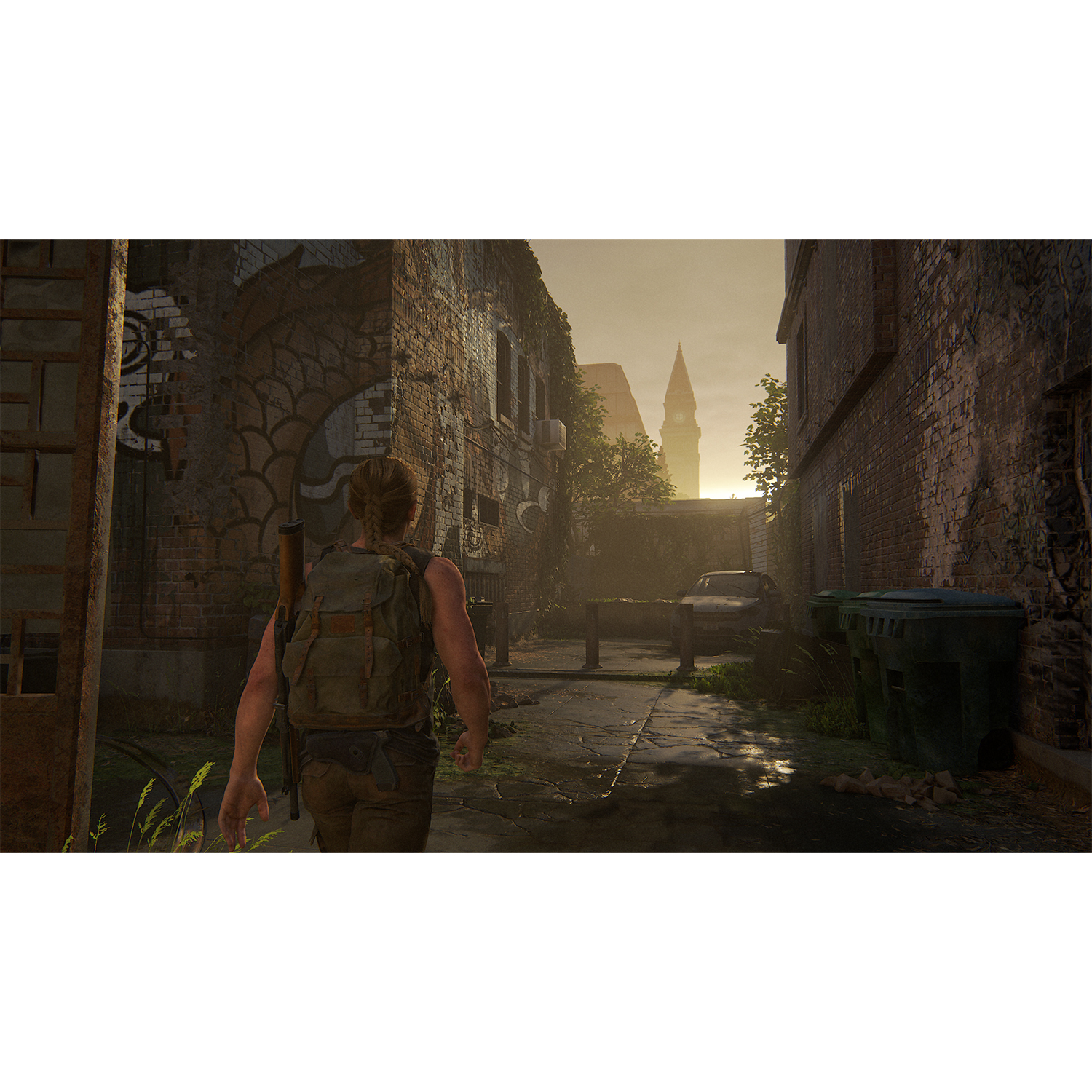 Una persona che cammina per una strada con edifici in mattoni. Il cielo è luminoso. La scena di gioco è Last of Us 2.