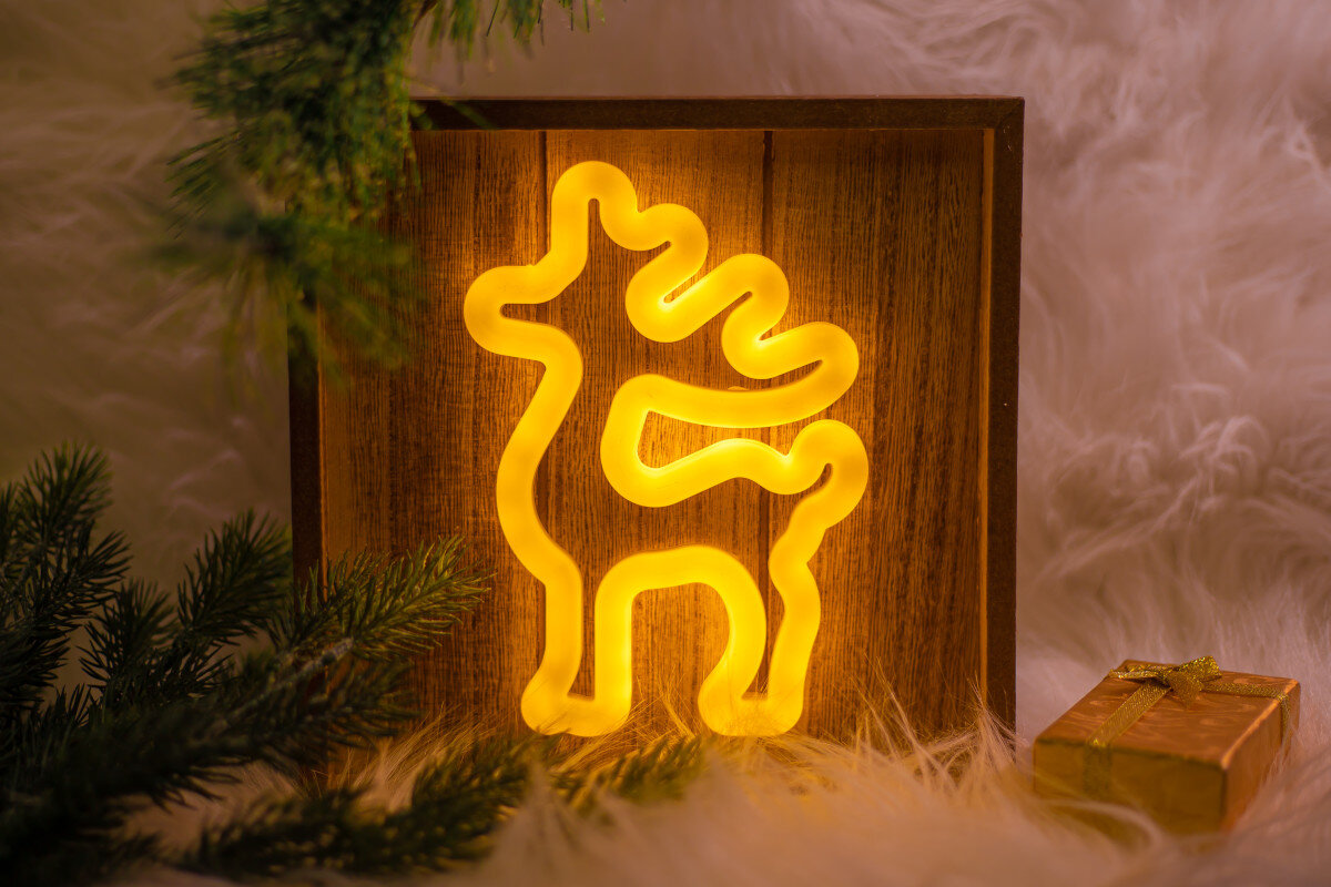 Ozdoba świąteczna z neonowym reniferem w drewnianej ramie.