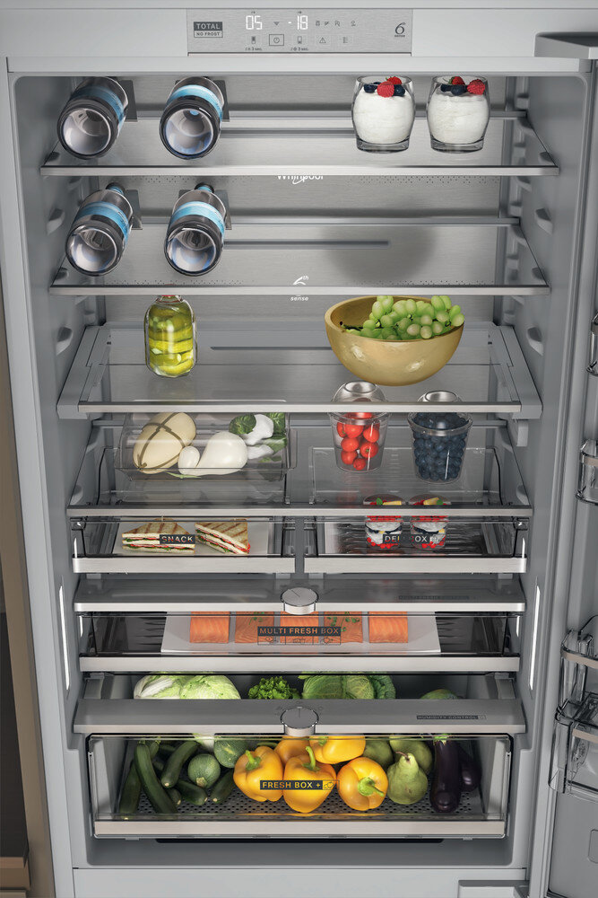 Wnętrze lodówki z produktami spożywczymi, w tym butelkami, słoikami, owocami i warzywami.