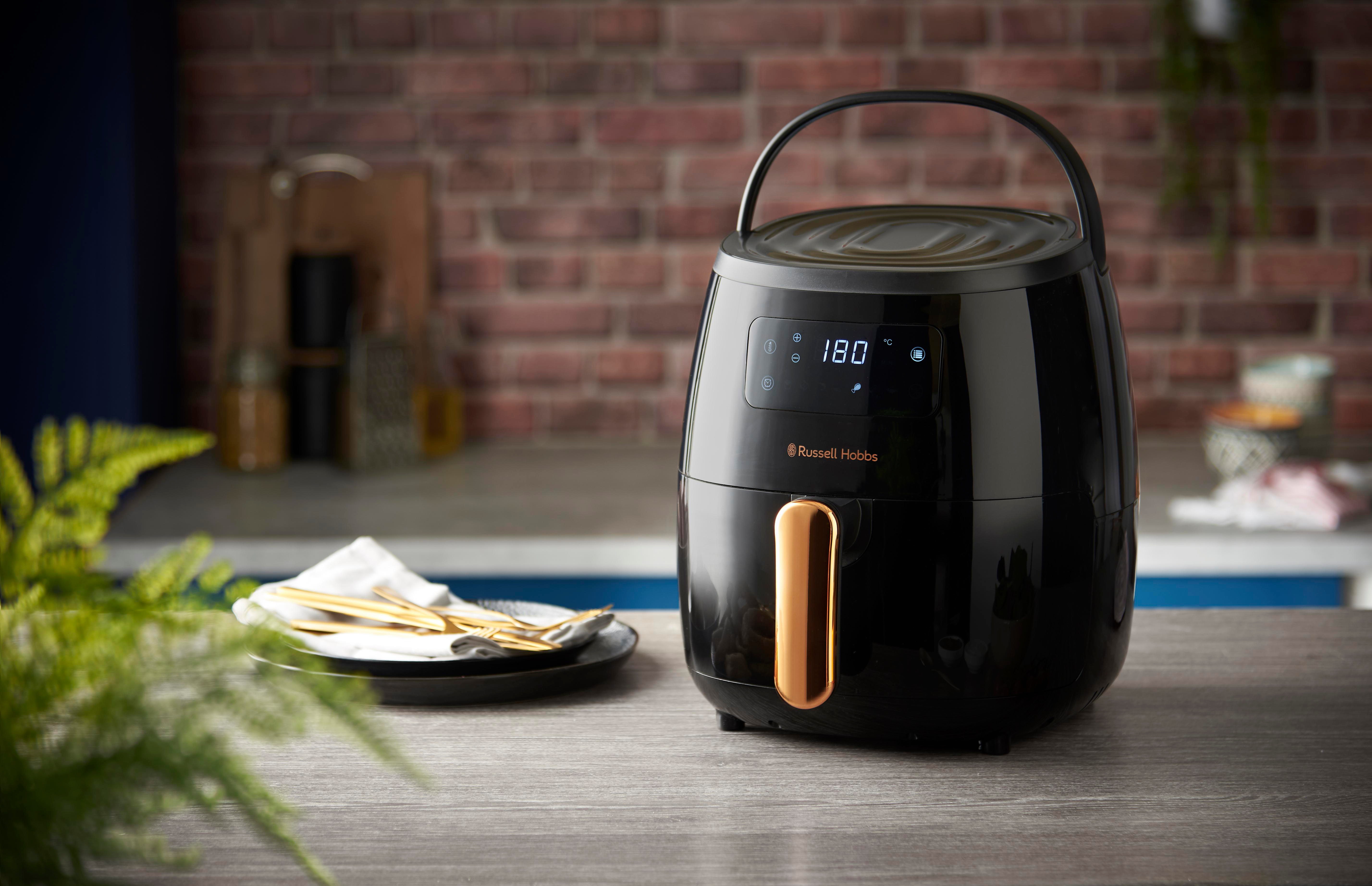 Schwarze Heißluftfritteuse auf einer Arbeitsplatte. Das Display zeigt Einstellungen. Marke Russell Hobbs.
