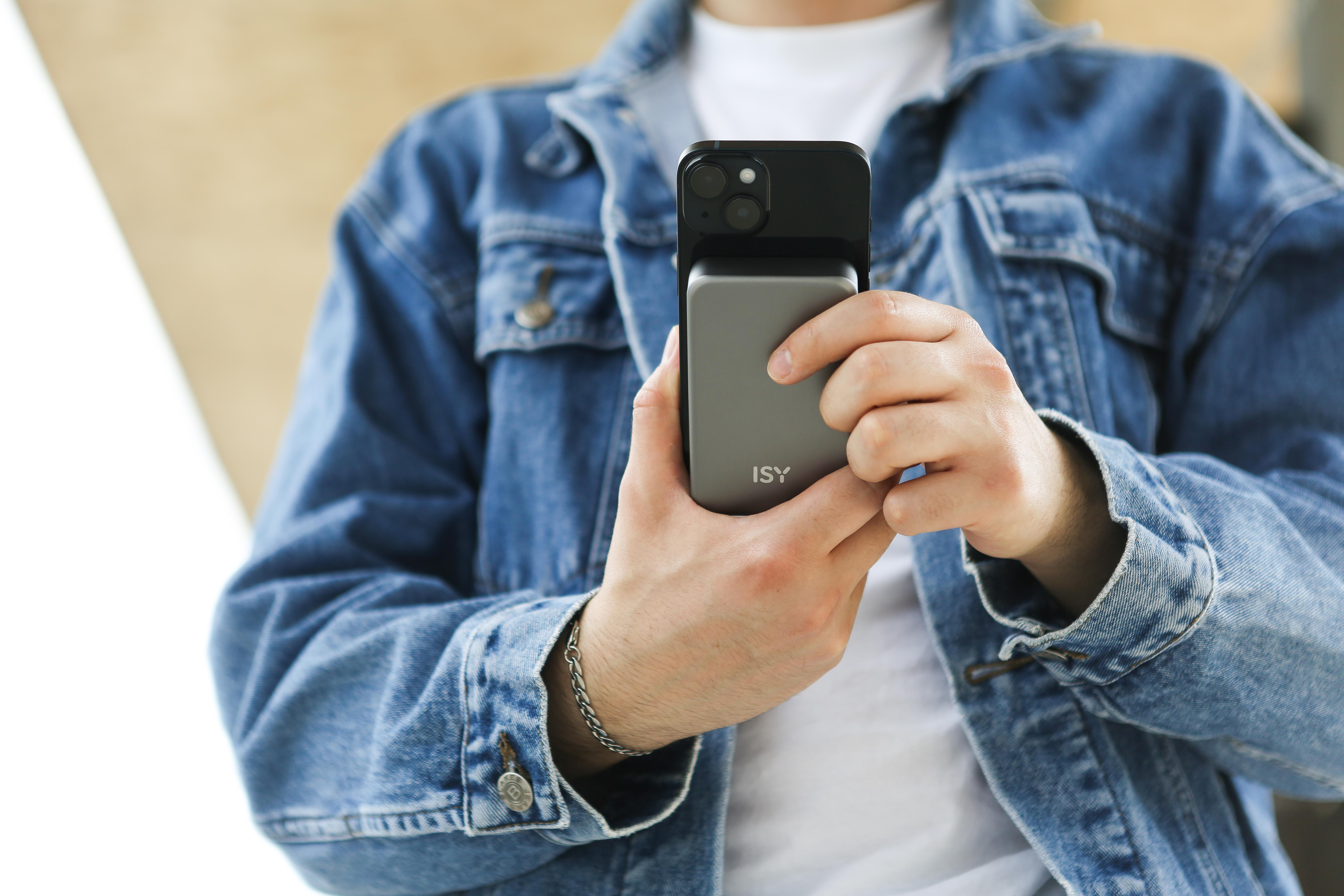 Person in Jeansjacke hält Telefon mit Ladehülle, Hände im Bild.
