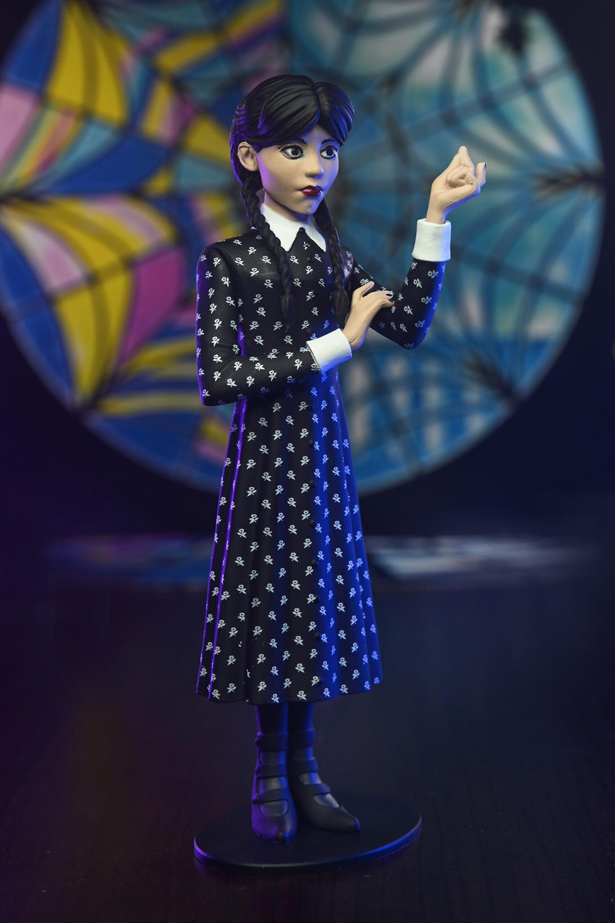 Eine Wednesday Addams-Figur in einem schwarzen Kleid steht auf einem runden Ständer.