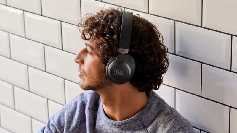 Ein Mann mit schwarzen JBL-Kopfhörern, der vor einer weiß gefliesten Wand sitzt und nach links schaut.