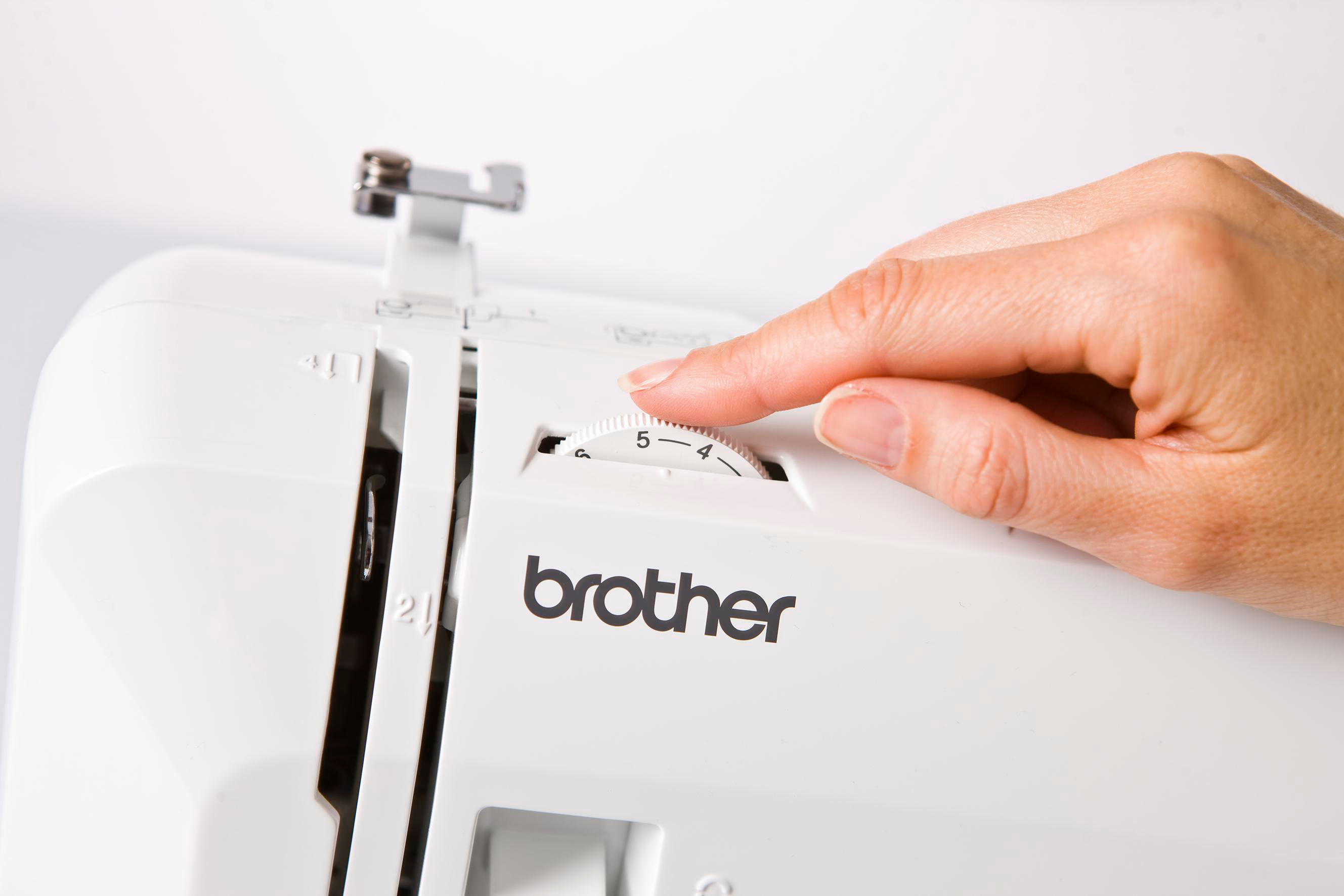 Eine Hand dreht einen Knopf an einer weißen Brother-Nähmaschine.