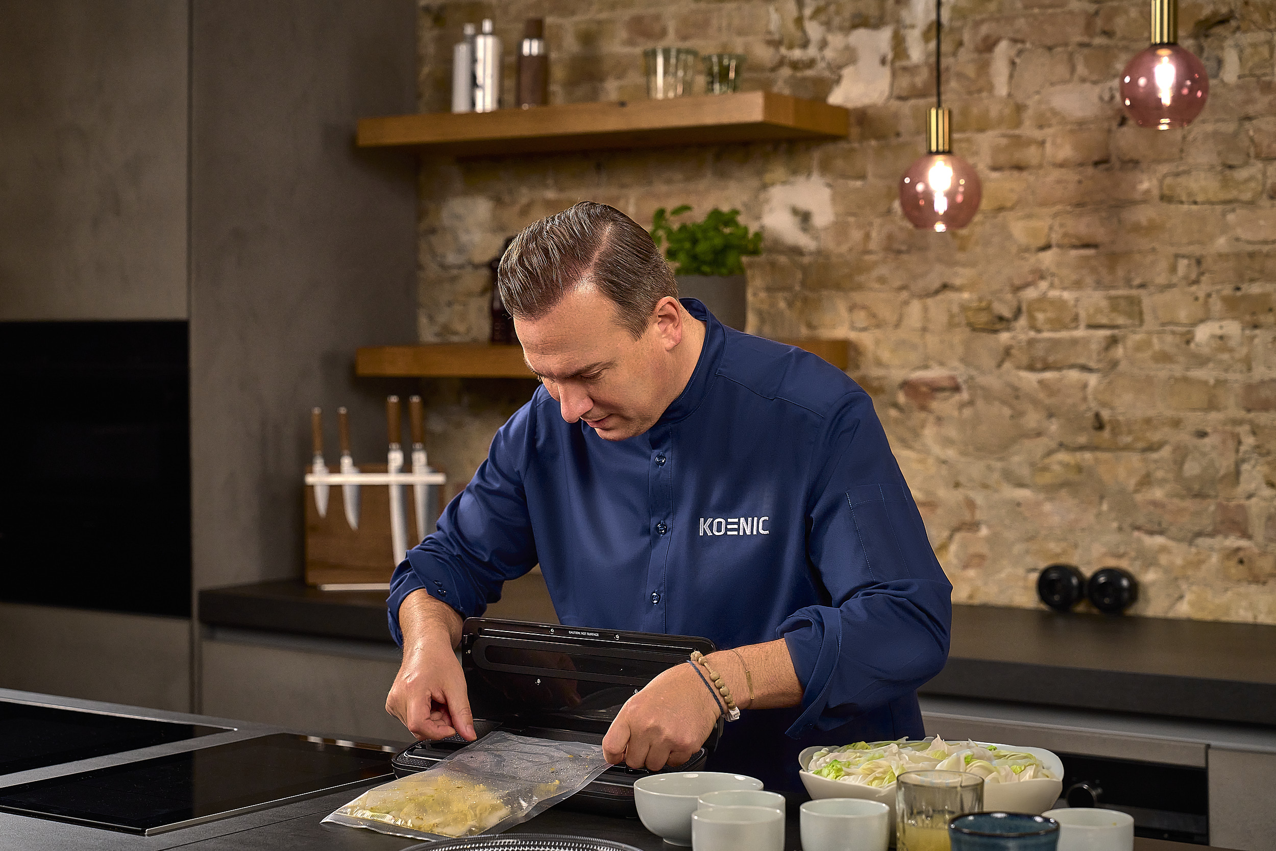 Koch in blauer Uniform verwendet ein Vakuumiergerät mit Zutaten daneben.