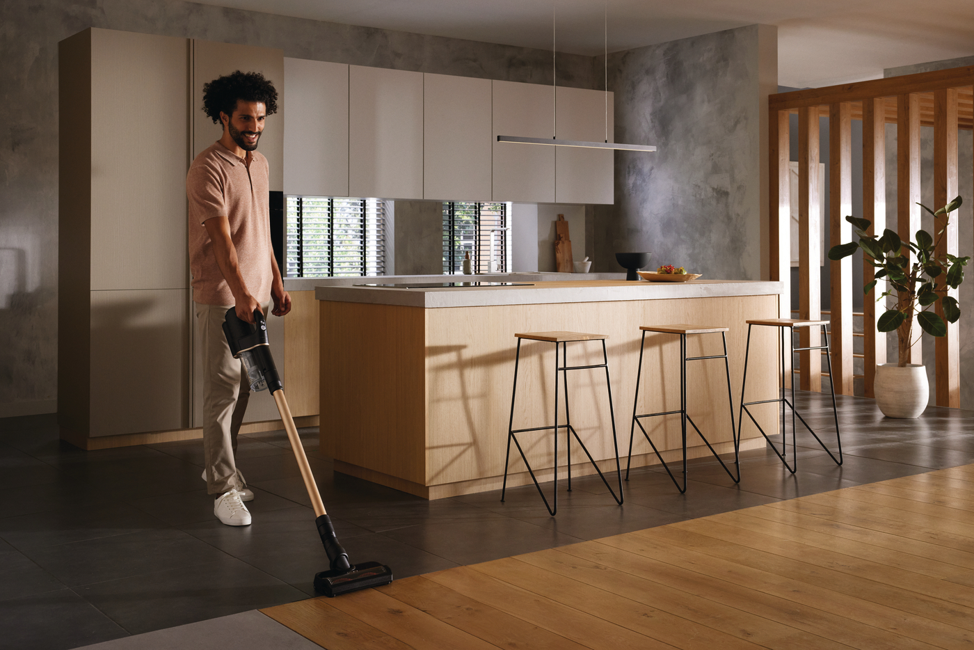 Ein Mann saugt einen Holzboden in einer modernen Küche. Weiße Schränke und eine Arbeitsplatte sind im Hintergrund.