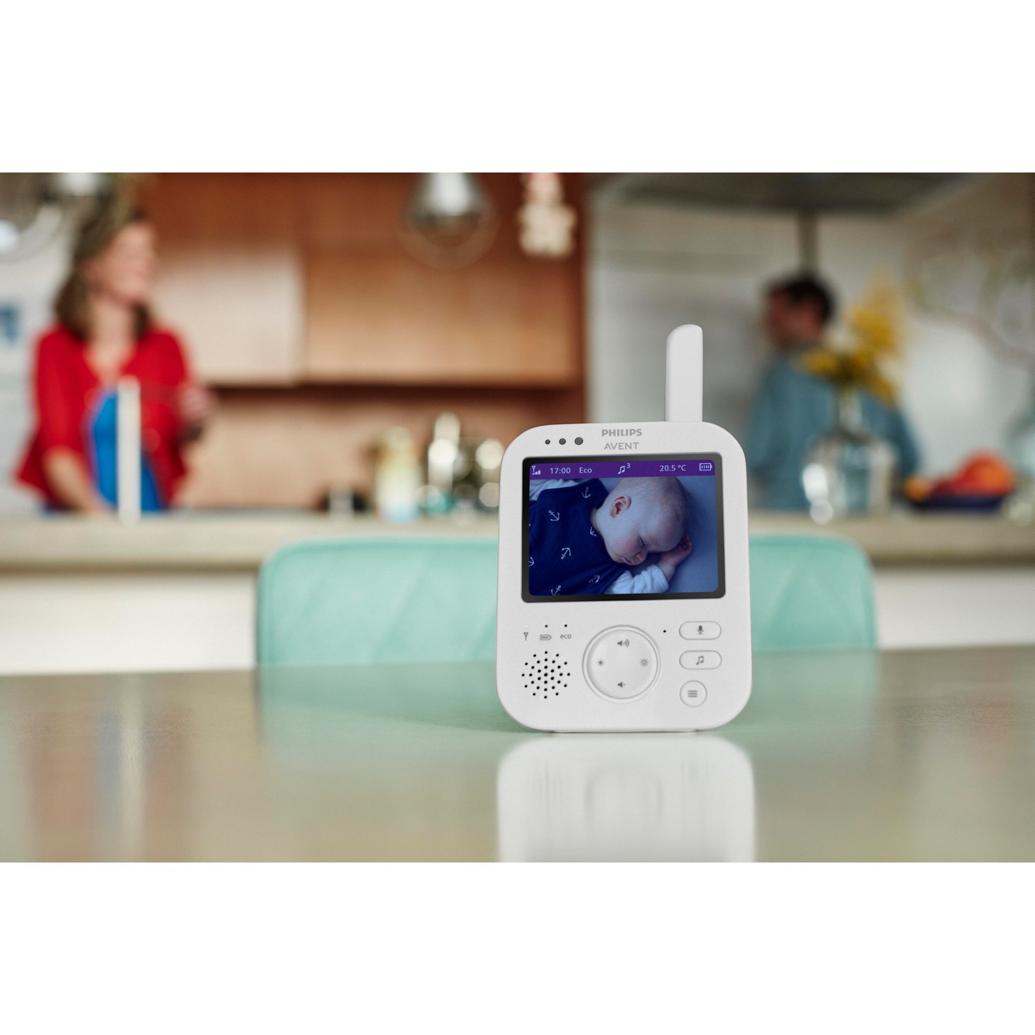 Babymonitor met een slapende baby. Twee mensen zijn wazig op de achtergrond.