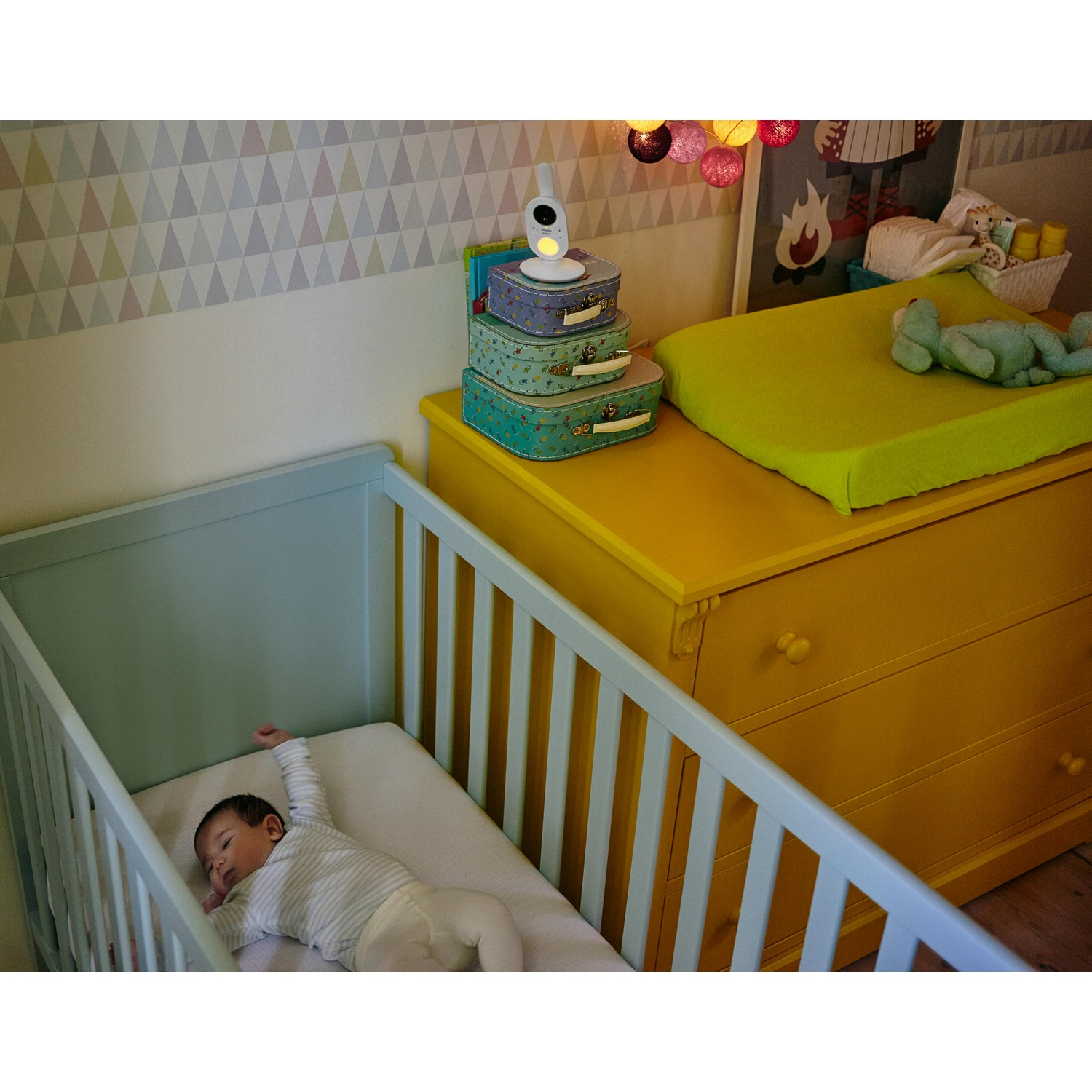 Baby slaapt in een wieg, met een aankleedtafel en decoraties op de achtergrond.