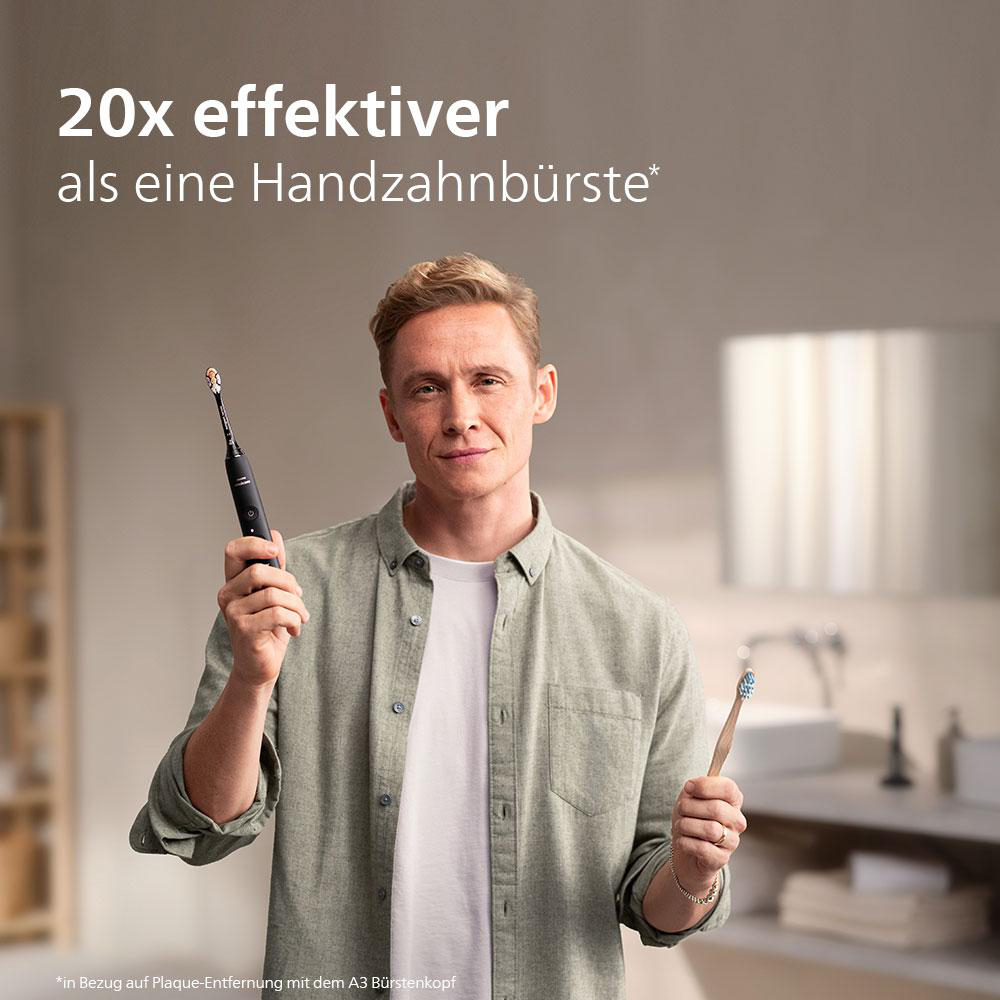 Ein Mann hält eine elektrische Zahnbürste und eine Handzahnbürste und lächelt in die Kamera.