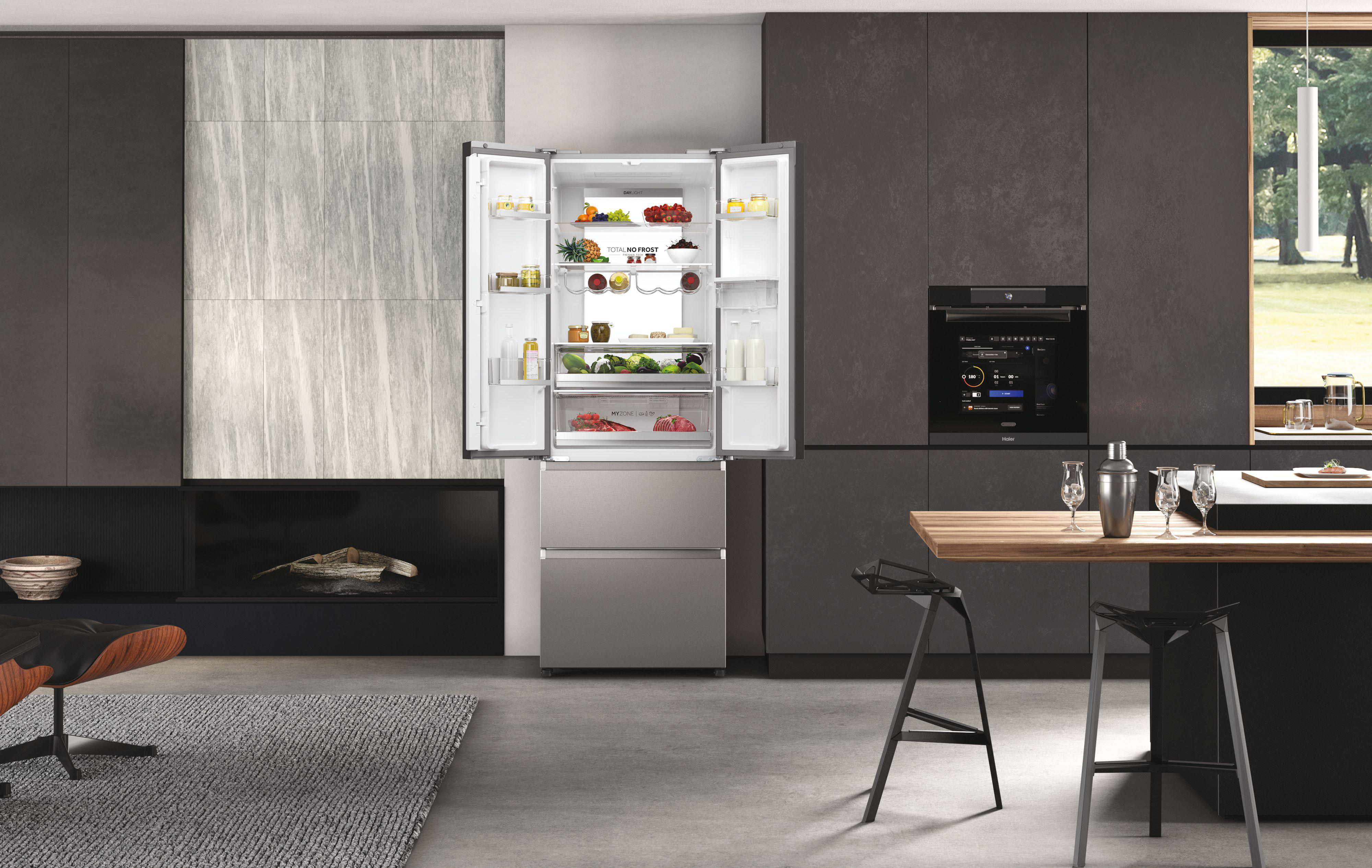 Kücheninterieur mit offenem Haier-Kühlschrank, der Lebensmittel zeigt. Essgruppe und Dekoration im Hintergrund.